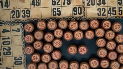 Cinematic-close-up-smooth-shot-from-above-of-a-pile-of-Bingo-wooden-barrels-in-a-square,-woody-figures,-old-numbers-background,-vintage-board-game,-slow-motion-120-FPS-commercial-gimbal-tilt-down