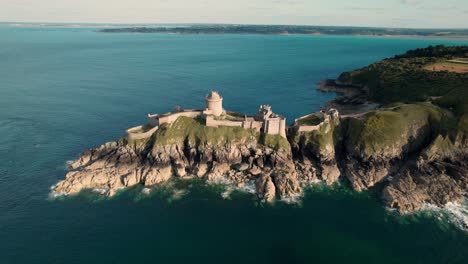 Drone-shot-with-Fort-La-Latte,-Chateau-de-la-Roche-Guyon-in-the-foreground-and-revealing-the-emerald-coast-in-the-background-near-cap-Frehel-in-Brittany,-France-on-a-sunny-day-of-summer