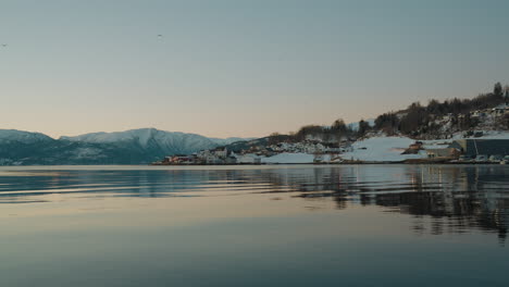 Blick-Auf-Den-Ytre-Samla-Fjord-In-Norwegen-Mit-Klarem-Wasser,-Schneebedeckten-Bergen-Auf-Der-Anderen-Seite-Des-Wassers-Und-Häusern-Im-Winterschnee