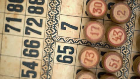 Cinematic-close-up-smooth-rotating-shot-from-above-of-Bingo-wooden-barrels-in-a-row,-woody-figures,-old-numbers-background,-vintage-board-game,-slow-motion-120-fps-commercial-gimbal-video