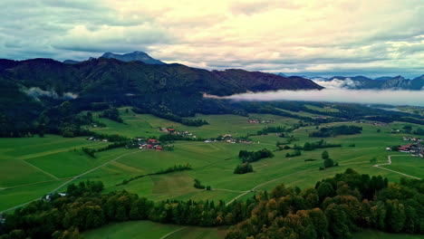 Aerial-drone-forward-moving-shot-over-green-farmlands-surrounded-by-mountain-range-on-all-sides-in-Norway-on-a-cloudy-day