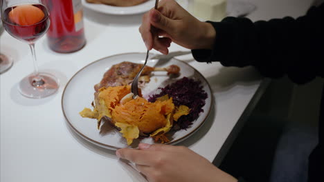 Woman-uses-fork-to-eat-sweet-potato-with-butter,-roasted-duck,-red-cabbage,-enjoying-festive-meal-with-red-wine,-healthy-balanced-diet,-homemade-food,-Christmas-dinner,-delicious-warm-dish,-close-up
