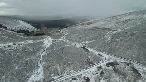 Winding-road-through-a-snow-dusted-landscape,-with-overcast-skies,-aerial-view