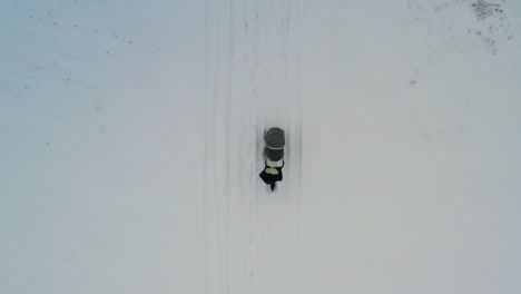 Aerial-top-down-view-of-female-push-baby-carriage-on-snowy-countryside-road