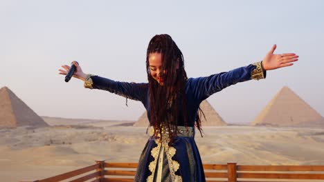 A-singer-performs-on-a-stage-in-front-of-audience-overlooking-pyramids,-Giza-in-Egypt-Arc-shot