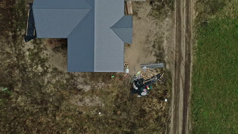 -Rural-homestead-with-a-corrugated-metal-roof,-adjacent-dirt-road,-clear-day-drone-footage