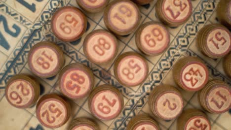 Cinematic-close-up-smooth-rotating-zoom-out-shot-from-above-of-Bingo-wooden-barrels-in-a-row,-woody-figures,-old-numbers-background,-vintage-board-game,-slow-motion-120-fps-commercial-gimbal-video