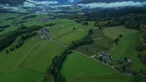 Countryside-with-scattered-houses,-fields-and-distant-misty-mountains,-overcast-skies-from-aerial-view