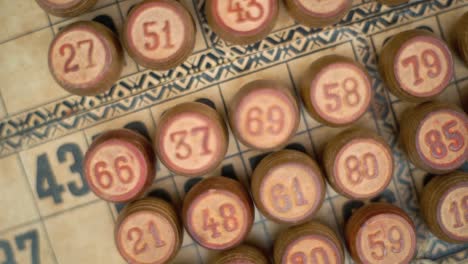 Cinematic-close-up-smooth-zoom-in-rotating-shot-from-above-of-Bingo-wooden-barrels-in-a-row,-woody-figures,-old-numbers-background,-vintage-board-game,-slow-motion-120-fps-commercial-gimbal-video