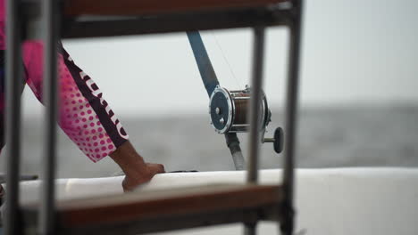 Man-holds-on-the-the-edge-of-the-boat,-near-the-fishing-rod-on-a-gloomy-overcast-morning-at-high-sea