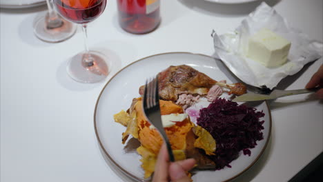 Woman-has-healthy-dinner-at-home,-using-fork-and-knife,-cutting-meat,-roasted-duck-leg,-sweet-potato,-red-cabbage,-balanced-diet,-festive,-delicious-meal,-homemade-dish,-enjoying-food-with-red-wine