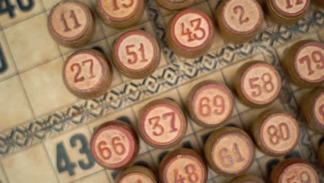Cinematic-close-up-smooth-rotating-zoom-in-shot-from-above-of-Bingo-wooden-barrels-in-a-row,-woody-figures,-old-numbers-background,-vintage-board-game,-slow-motion-120-fps-commercial-gimbal-video