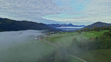 Early-mysterious-misty-morning-fog-over-green-wonderful-panoramic-valley,-tall-mountains-in-background