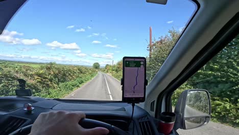 Driver's-perspective-of-a-sunny-country-road-with-GPS-navigation,-clear-blue-sky