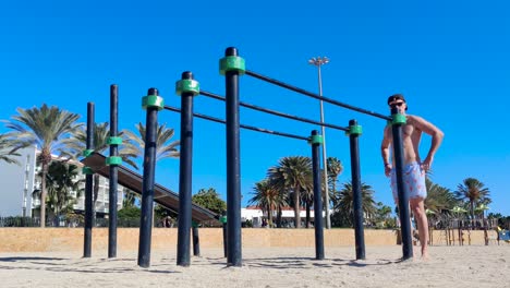 man-doing-a-bar-dip-workout-at-a-sunny-beach,-fit-caucasian-male-training-calisthenics,-shot-in-fuerteventura