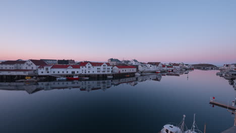 Sunrise-in-Henningsvær,-Lofoten-Islands,-Norway,-showcasing-the-fishing-village,-homes-along-the-water,-with-a-pink-and-blue-sky,-seagulls,-and-smooth-water-reflecting-the-sky