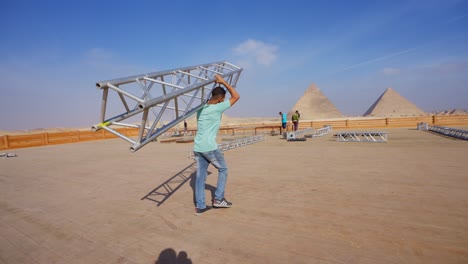 people-prepare-the-stage-for-a-party-in-the-desert-beside-the-Pyramids,-Giza-in-Egypt,-Establishment-shot,-tracking-shot