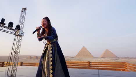 A-singer-performs-on-a-stage-in-front-of-audience-overlooking-pyramids,-Giza-in-Egypt-push-in-shot