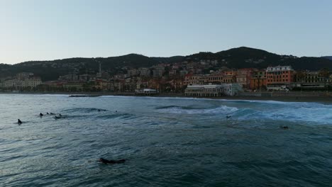 Group-of-surfers-riding-waves-at-sunset-with-Varazze-coastline-in-background