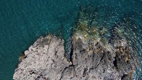 Rising-Aerial-Top-View-over-Mediterranean-Seashore-Rocks-and-Blue-Waters