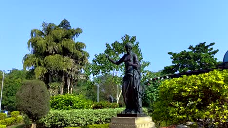 Panorámica-De-Cámara-Amplia-En-Un-Jardín-Con-Cenador-En-El-Fondo-De-Una-Estatua-De-Mujer-En-Sayaji-Baugh-En-La-Ciudad-De-Vadodara,-India
