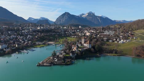 Spiez-on-Lake-Thun-with-marina-and-Alps-in-the-background,-clear-sky,-aerial-view