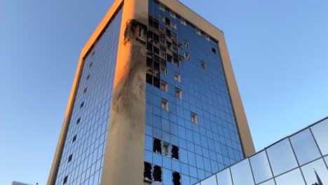 Rockets-bombed-and-destroyed-tall-skyscraper-building-with-broken-glass-windows-on-Solomianska-Street-in-Kyiv-Ukraine,-critical-war-damage-in-the-city-capital,-Russia-attacks-Ukraine,-4K-tilting-down