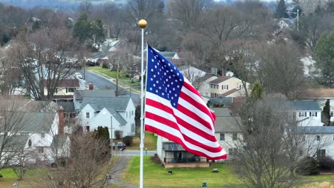 Aerial-close-up-of-American-flag-waving-over-suburban-neighborhood-houses