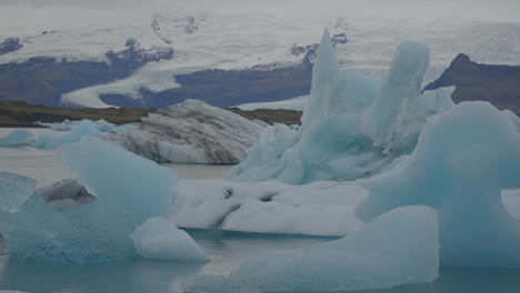 Gletscher-Schwimmen-In-Der-Gletscherlagune,-Island,-Mit-über-Ihnen-Fliegenden-Möwen,-Vor-Dem-Hintergrund-Des-Blauen-Wassers,-Das-Sich-In-Richtung-Diamond-Beach-Bewegt