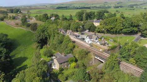 Aerial-footage-of-Clapham-train-station,-railway-line,-stone-railway-bridge-and-river-in-rural-Yorkshire,-UK