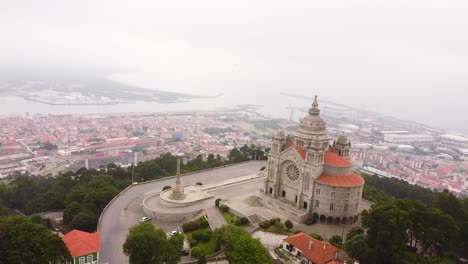 Iconic-church-on-hilltop-with-city-of-Viana-do-Castelo-bellow,-aerial-orbit-view