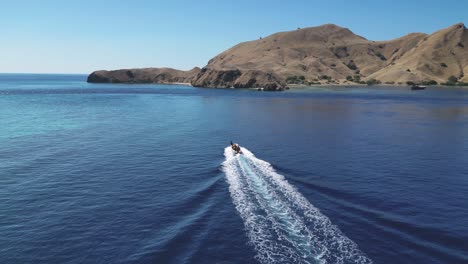Drone-following-and-descending-over-a-speedboat-racing-towards-a-dry-and-barren-island