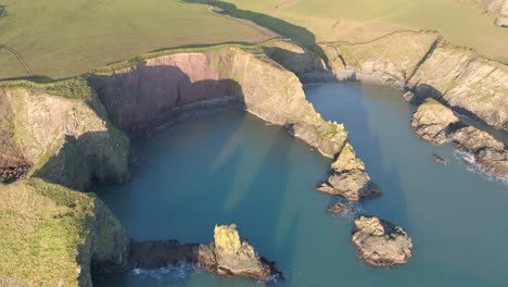 Drone-winter-afternoon-sunshine-of-hidden-beach-and-sheltered-bay-on-The-Copper-Coast-Waterford-Ireland
