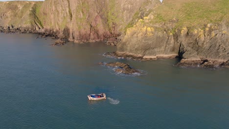 Drone-cinematic-fishing-boat-under-cliffs-at-Copper-Coast-Waterford-Ireland