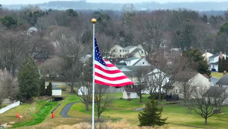 Aerial-close-up-of-American-flag-waving-over-suburban-neighborhood