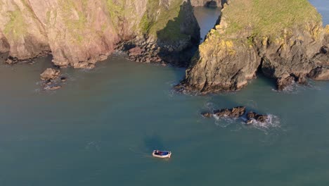 Barco-De-Pesca-Estático-Con-Drones-Trabajando-Bajo-Acantilados-Y-Cuevas-Marinas-Costa-De-Cobre-Waterford-Irlanda-Impresionante-Ubicación
