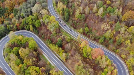 Truck-delivering-timber-and-cars-on-asphalt-winding-motorway-through-autumn-woods
