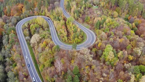 Cars-on-modern-country-roadway,-remote-route-in-fall-foliage-woodland-aerial-panorama