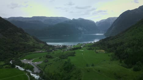 Drohne-Fliegt-Durch-Ein-Tal-Zu-Einem-Kleinen-Norwegischen-Dorf-An-Einem-See