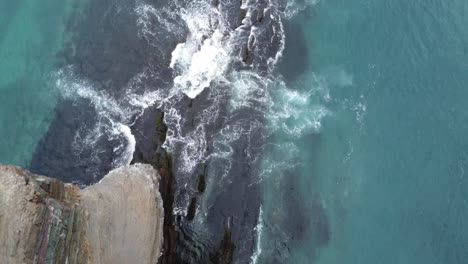 Drone-shot-going-over-the-edge-of-a-300ft-cliff-with-waves-crashing-against-the-coast-below