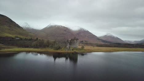 Aerial-orbiting-shot-of-famous-kilchurn-castle-at-lake-loch-awe-with-snowy-mountains-in-background---Cinematic-drone-flight