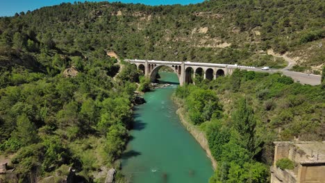 Murillo-de-Gallego-Bridge-in-Huesca-over-a-turquoise-river,-surrounded-by-lush-greenery,-aerial-view