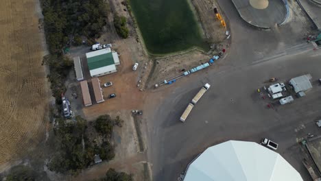 Aerial-top-down-show-of-industrial-cargo-truck-arriving-farm-with-large-silo-storage-in-Australia