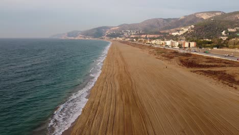 Long,-sandy-Castelldefels-Beach-in-Barcelona,-waves-gently-lapping-the-shore,-aerial-view