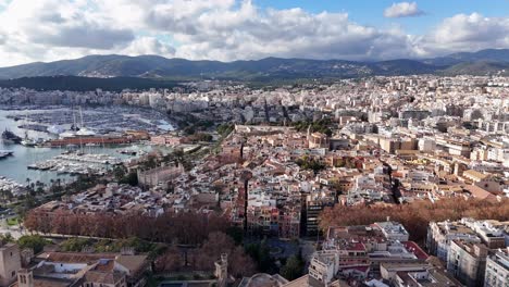 Aerial-establishing-shot-showing-Beautiful-historic-city-of-Palma-de-Mallorca-with-harbor-and-sailing-boats---Mountain-range-of-island-in-background---Spanish-neighborhood-in-capital