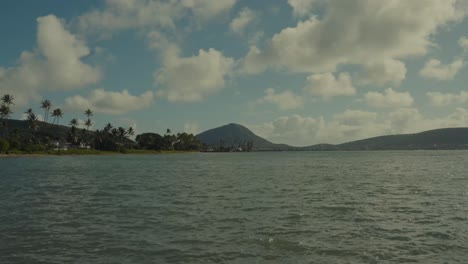 time-lapse-with-the-blue-water-of-the-Pacific-in-the-foreground-and-a-volcanic-island-mountain-and-palm-tree-lined-peninsula-grace-the-horizon-while-white-puffy-clouds-glide-across-the-blue-skies