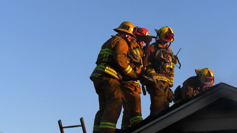 Firefighters-on-the-roof,-axeing-their-way-inside-a-smoking-house,-sunny-evening