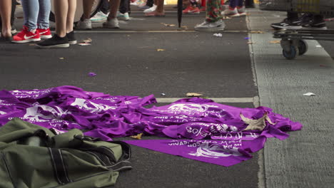 close-up-shot-of-political-purple-feminist-kerchiefs-for-sale-at-abortion-rally,-people-march-next-to-them