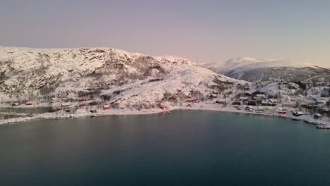 Ersfjordvegen-village-covered-in-snow-during-winter-with-calm-waters,-aerial-view