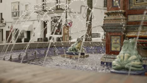 Scenic-view-of-traditional-fountain-with-frog-statues-spewing-water-up,-residential-buildings-in-background